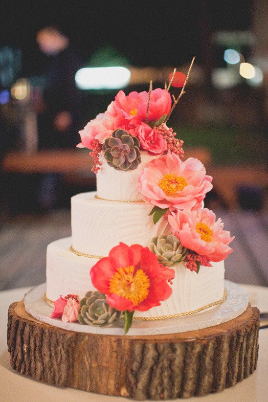 Elegant three-tiered wedding cake decorated with flowers on a wood base
