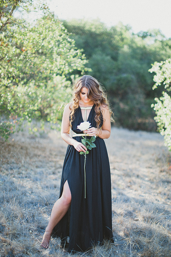 Woman in a black dress holding a white rose in nature scene