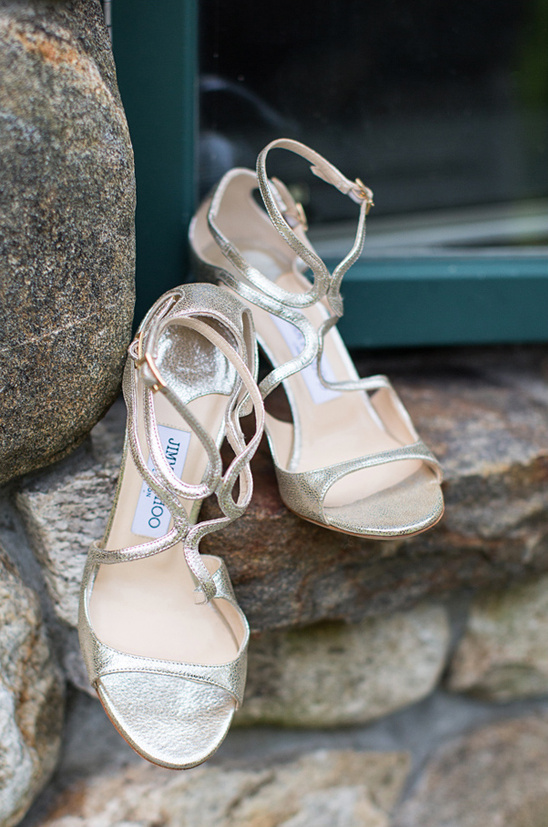 Elegant gold Jimmy Choo sandals on a rustic stone surface