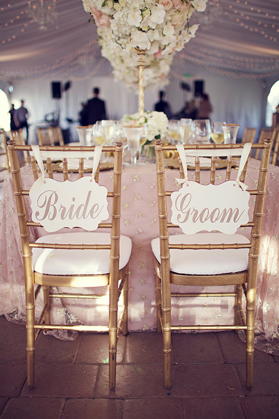 bride and groom signs on gold chairs