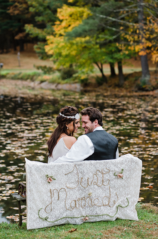 Newlyweds embrace on a bench by the lake, Just Married sign