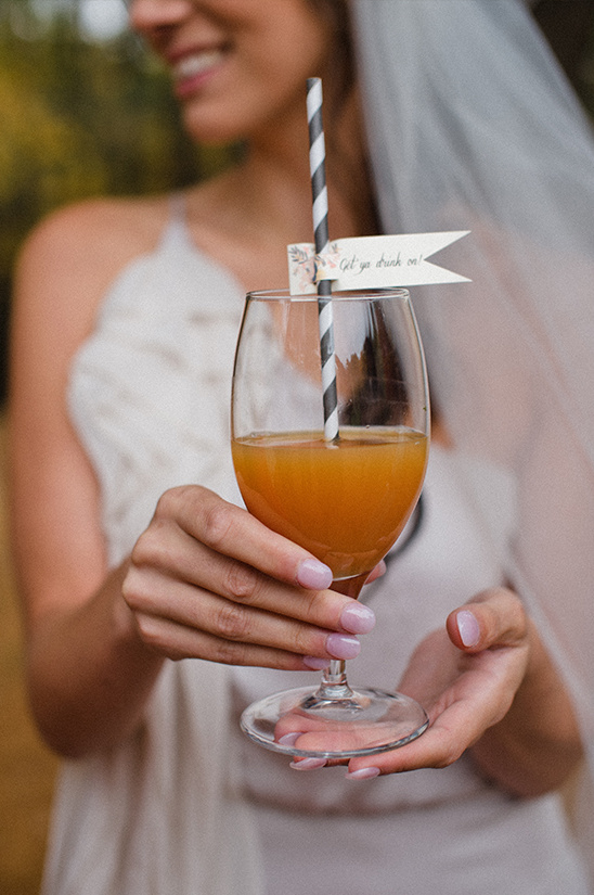 Bride with a drink cheers and a Get ye drunk on flag