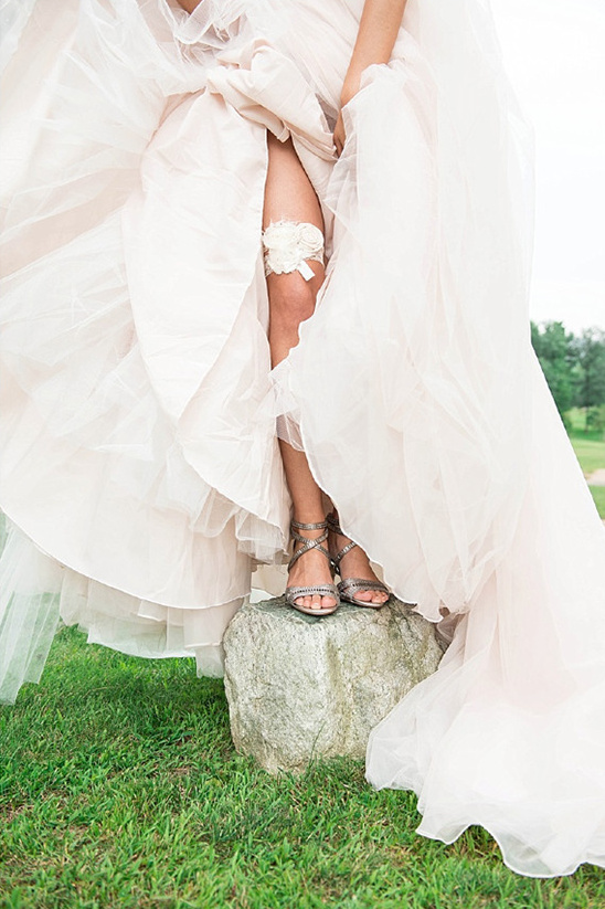 Bride in wedding dress with garter and silver sandals on a rock