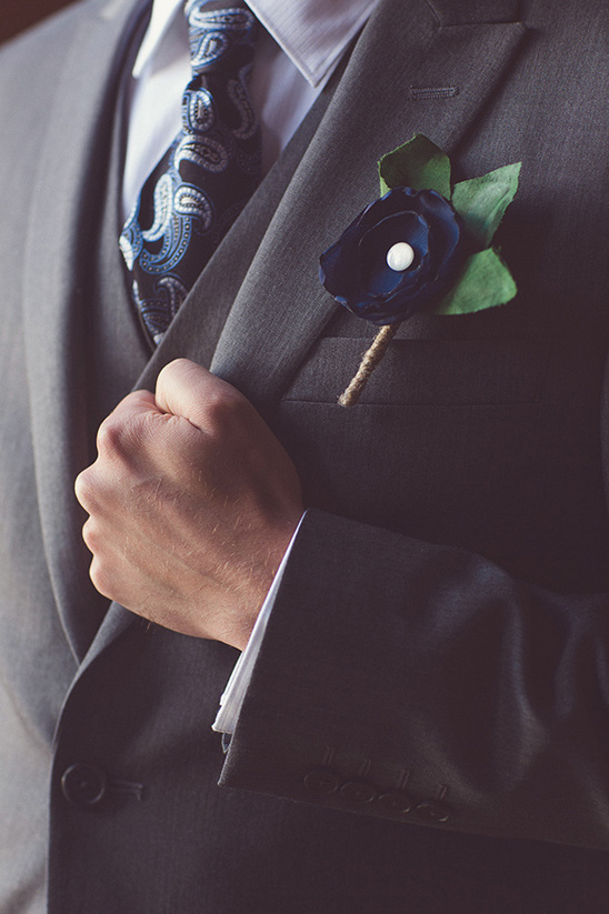 Groom adjusting suit jacket with navy flower boutonniere