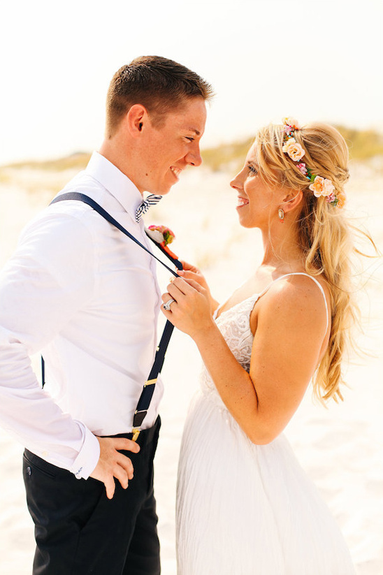 Happy bride adjusts groom suspenders at beach wedding