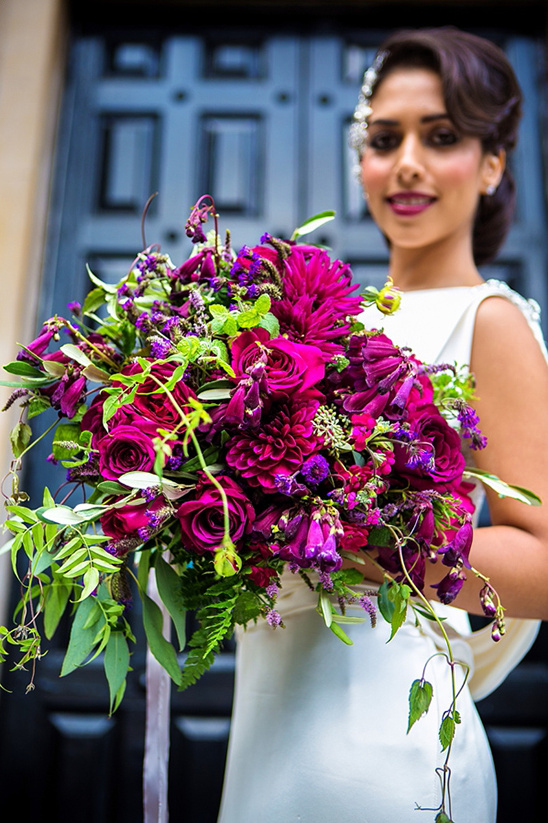 Beautiful bride smiles with vibrant purple wedding bouquet