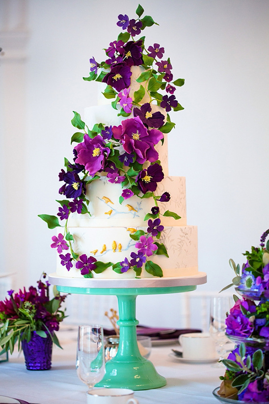 White wedding cake with purple flowers on green stand