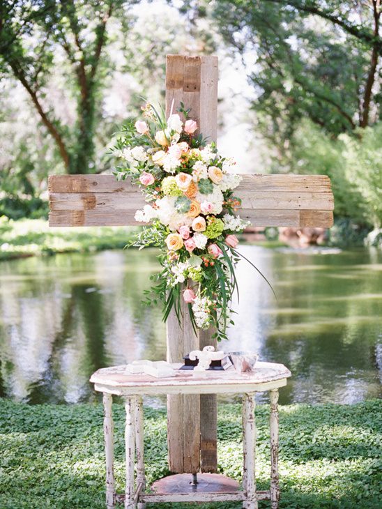 Wooden cross adorned with flowers at outdoor wedding altar