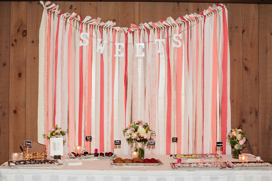 A beautifully decorated sweets table with a ribbon backdrop and treats