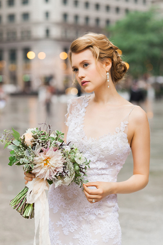 Bride in lace dress holding bouquet on city street