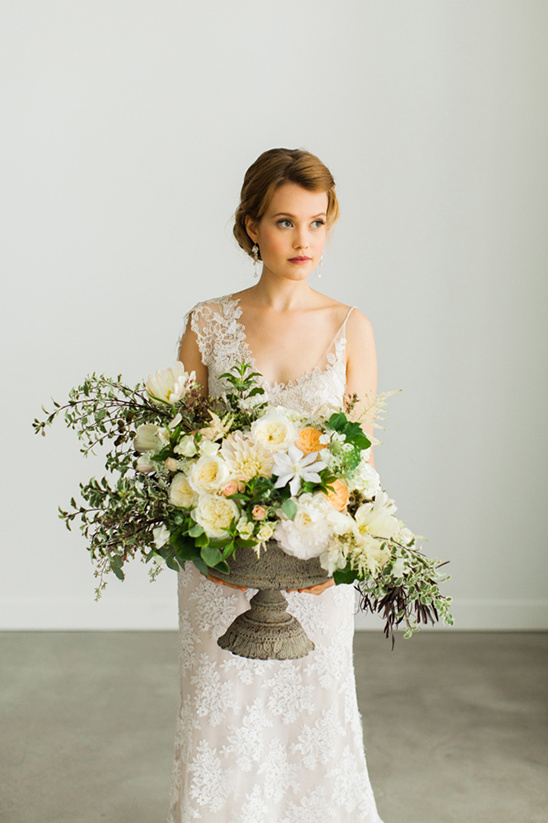 Bride in lace gown holding large floral arrangement