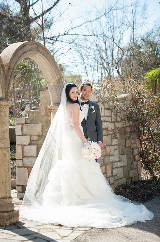 Happy bride and groom pose by stone archway wedding
