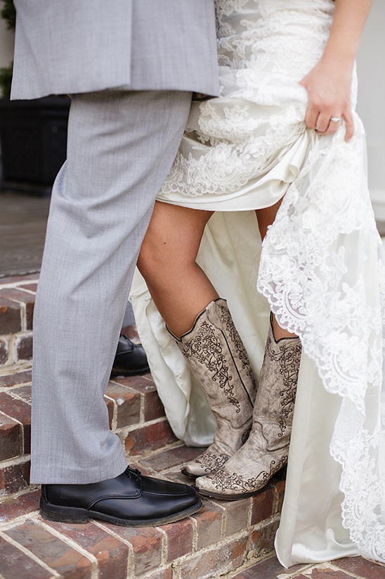 Bride in boots lifts dress near grooms shoe wedding style