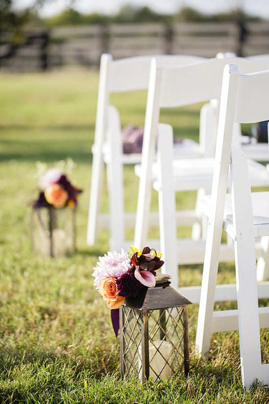 White wedding chairs and flower lanterns decorate lawn aisle