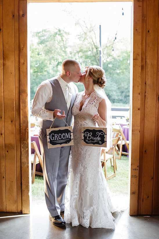 Bride and groom share a kiss holding Bride and Groom signs at wedding