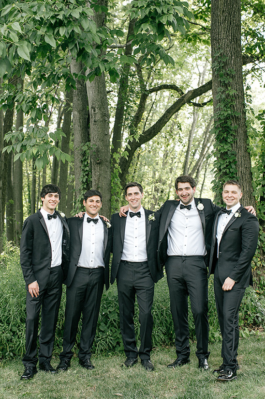 Wedding groomsmen in black tuxedos in green forest
