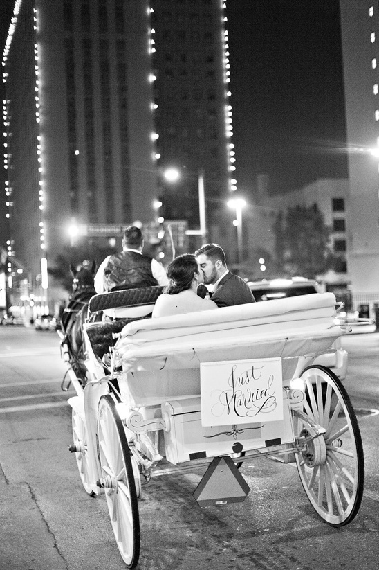 Newlyweds kiss in horse-drawn carriage with city lights at night