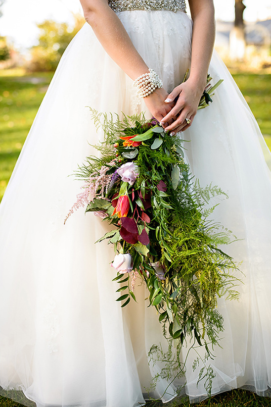 Bride in white gown holding a colorful cascading bouquet