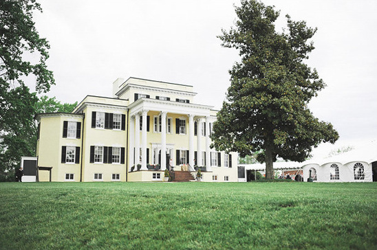 Yellow mansion with white columns green lawn and tents