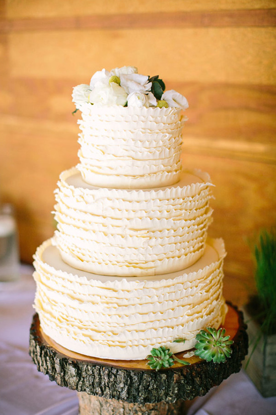 Elegant tiered wedding cake with floral top on a wood slice stand