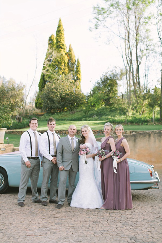 Wedding party posing with a vintage car on a sunny day