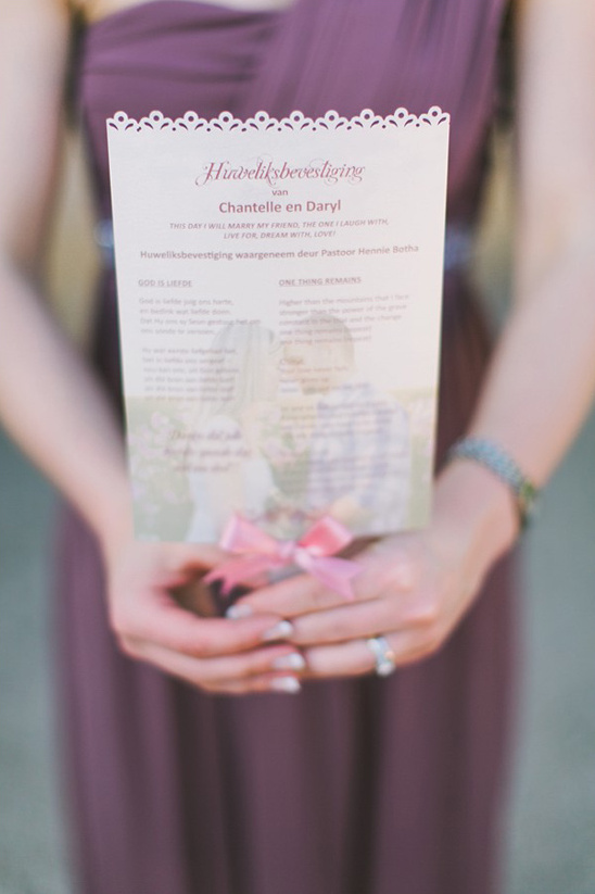 Wedding invitation held by someone in a purple dress, with pink bow