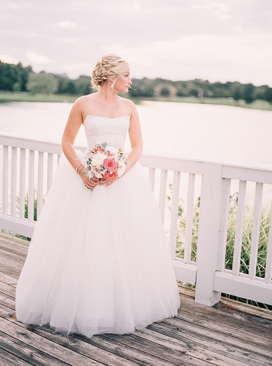 Elegant bride in white wedding dress holding flowers by the lake