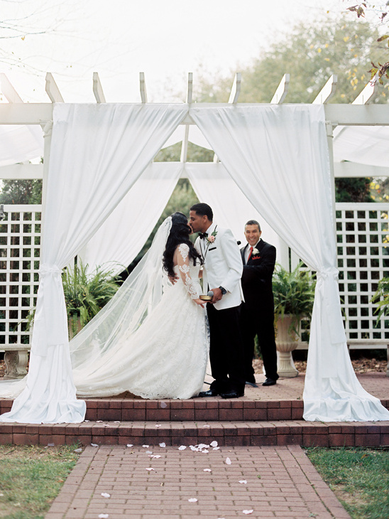 Couple shares a kiss during outdoor wedding ceremony under white draping
