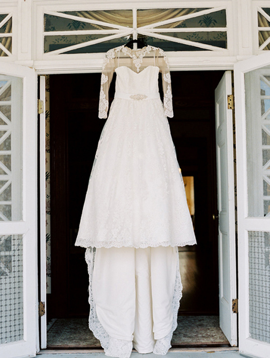 Elegant white lace wedding dress hanging in a doorway