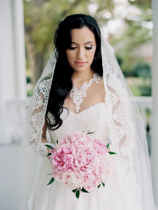Beautiful bride holding pink peonies in a white lace wedding dress