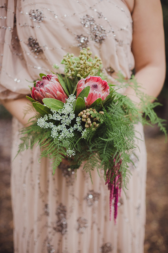 Woman in a dress holding a protea and green foliage bouquet