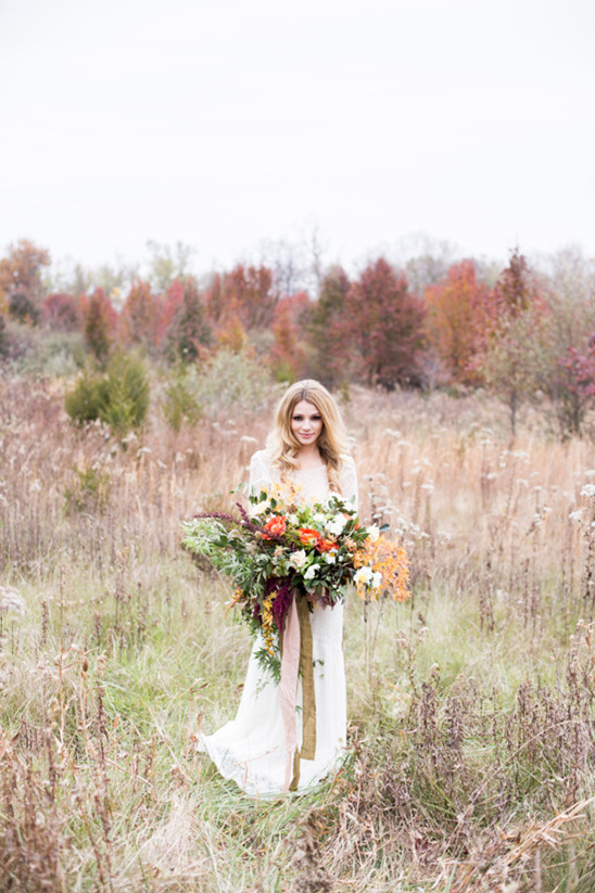 Bride in white dress holding fall bouquet in a field