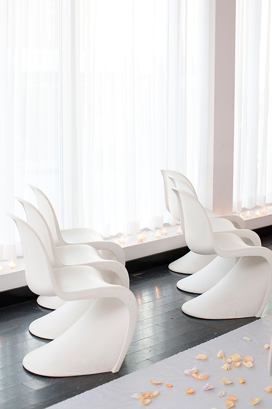 Modern white chairs arranged for a ceremony by a bright window
