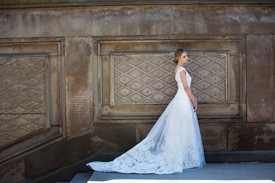 Elegant bride poses in a lace wedding dress outdoors in front of a wall