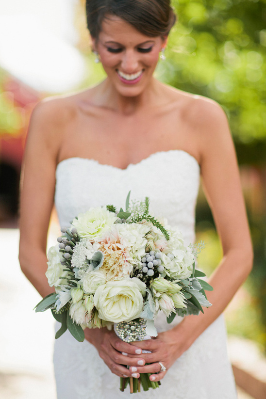 Bride in a white dress smiling holding a bouquet of white flowers