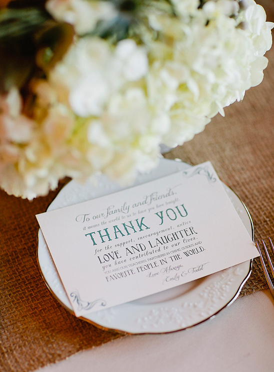 Wedding thank you card on plate with flower arrangement in the background