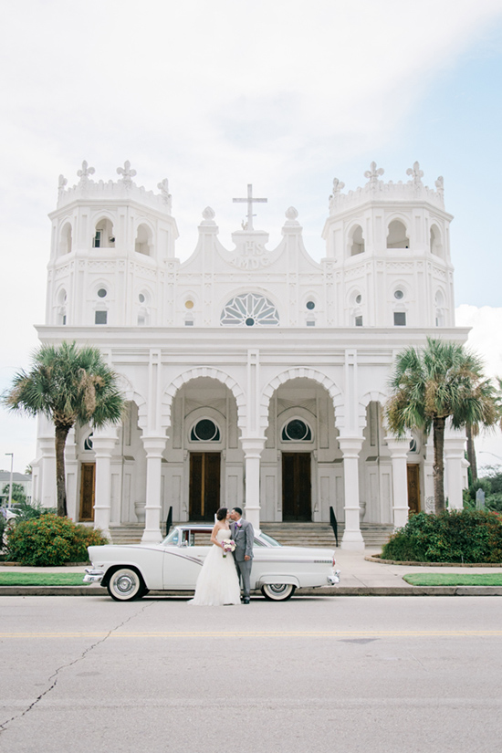 Newlyweds kiss by vintage car, white church backdrop