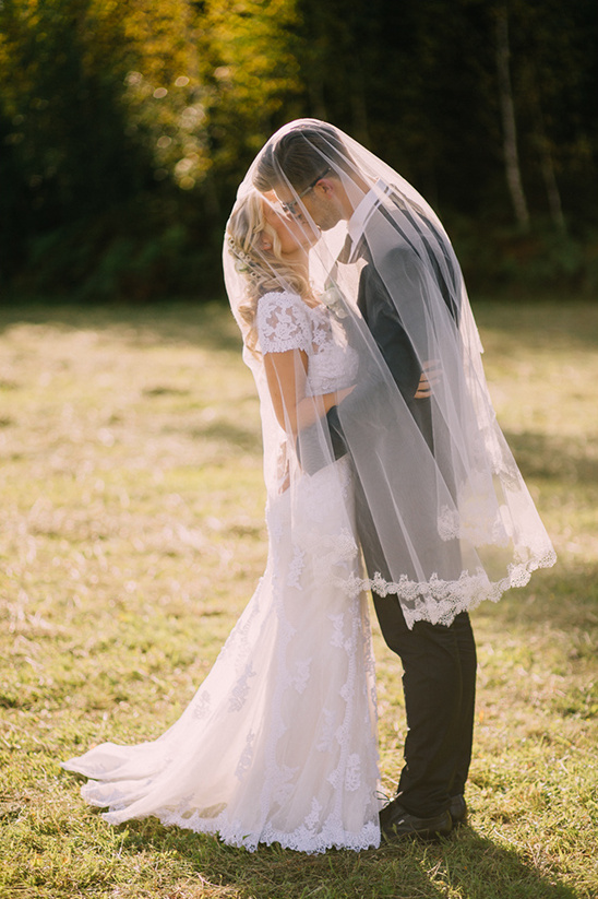 Bride and groom share a tender kiss under a wedding veil outdoors