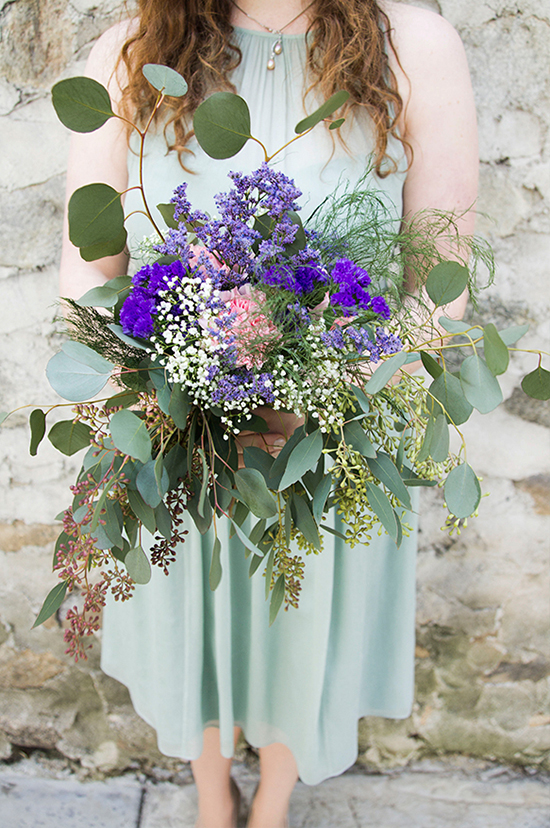 Woman in green dress holding a beautiful floral bouquet with greenery