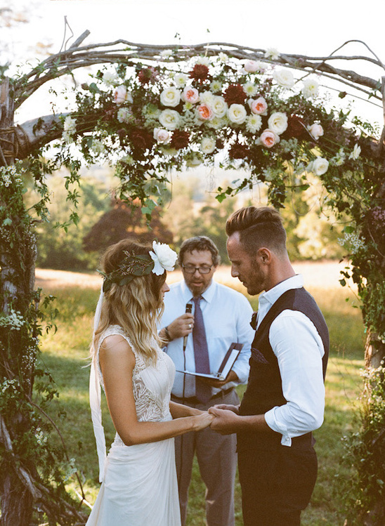 Bride and groom hold hands at outdoor floral wedding