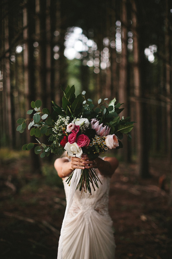 Bride hides behind stunning wedding bouquet in forest