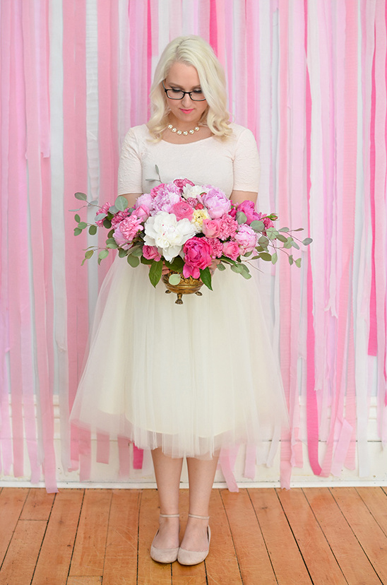 Blonde woman in dress holding large floral bouquet for event