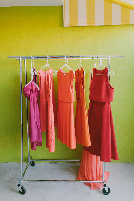 Bright dresses hanging on a rack against a green wall