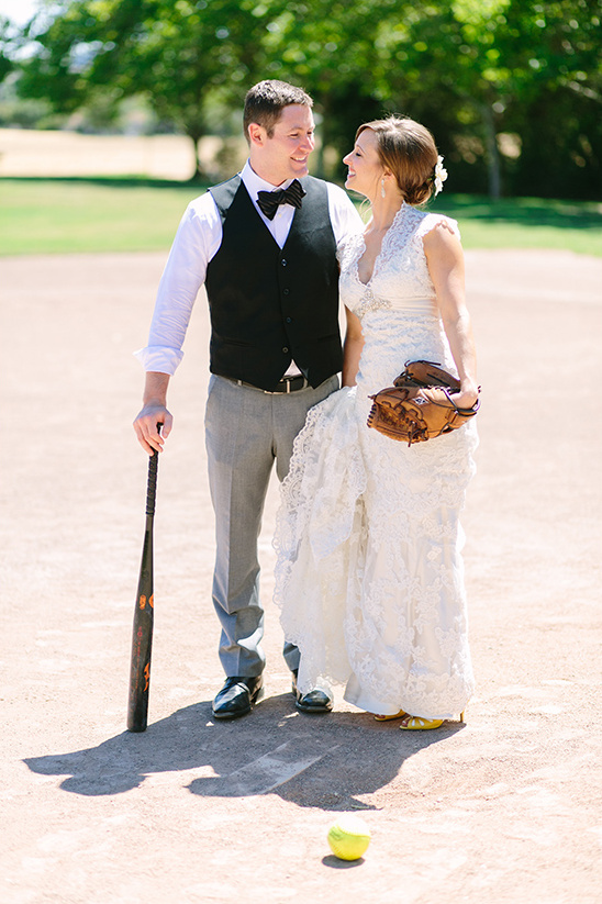 Newlyweds smiling at each other on a softball field, wedding day