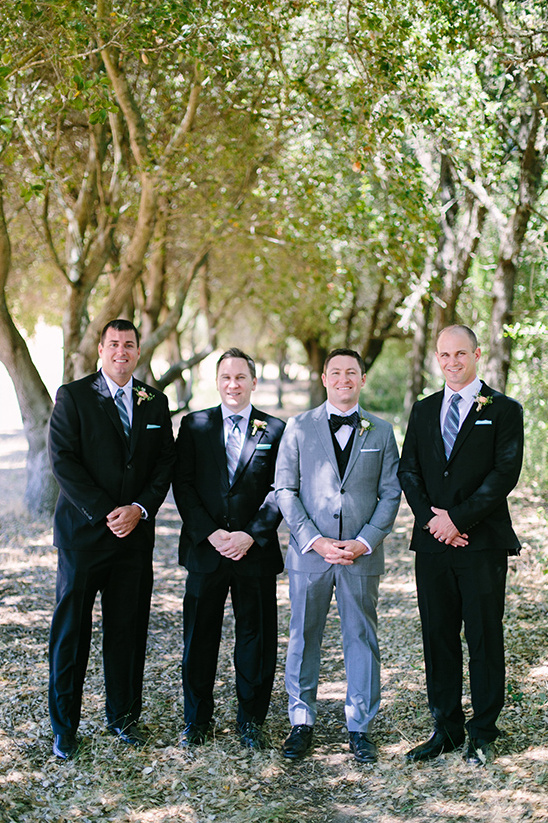 Groomsmen in suits standing in line under trees at a wedding