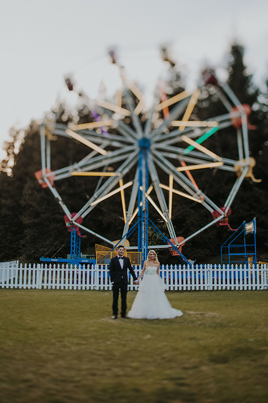 A newlywed couple holding hands in front of a Ferris wheel