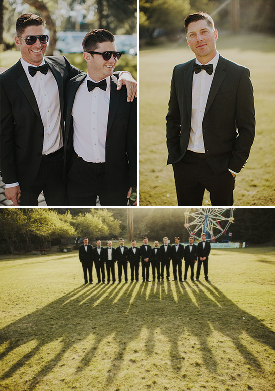 Groomsmen in black tuxedos pose outside in the warm sunlight