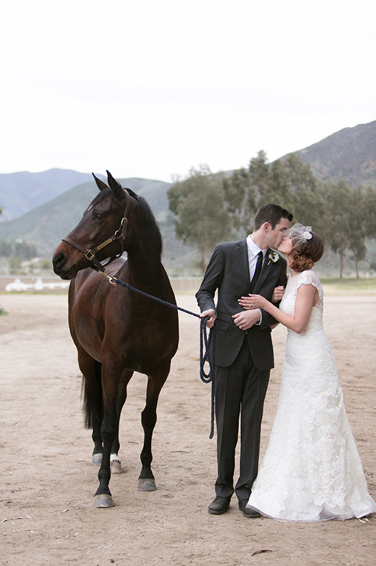Bride and groom kiss next to a horse on their wedding day
