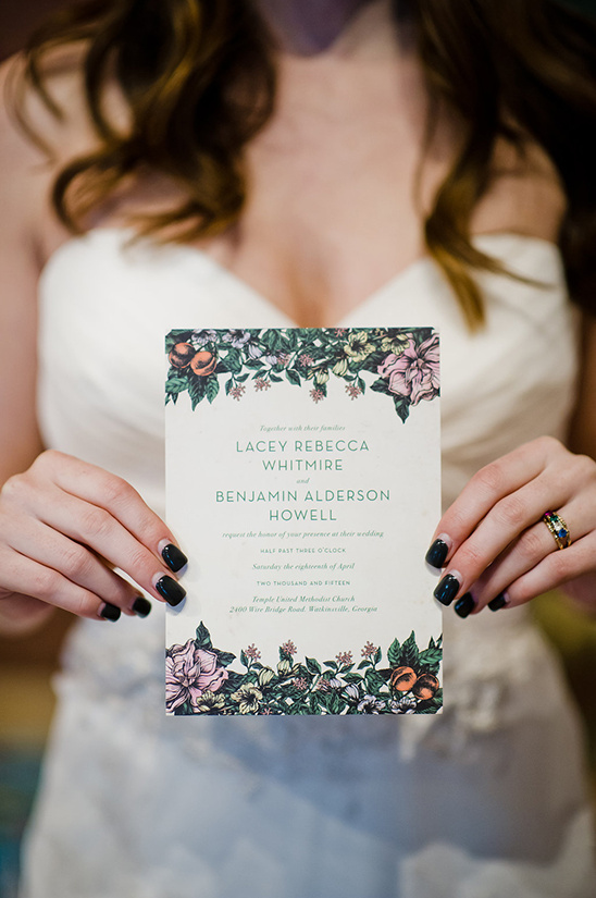 Bride holding a floral wedding invitation card with black nails