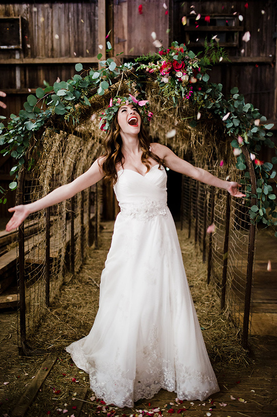 Joyful bride celebrates under a floral arch as petals fall around her